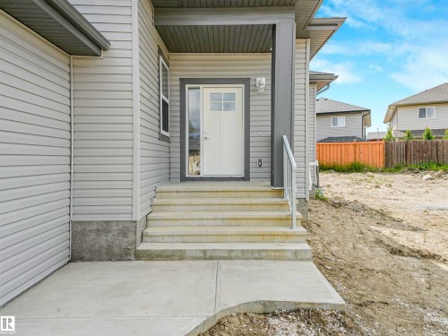Covered entryway with concrete steps and landing, featuring a white door with transom window and sidelight, and a white handrail - 22 Dalquist Bay, Leduc, AB 