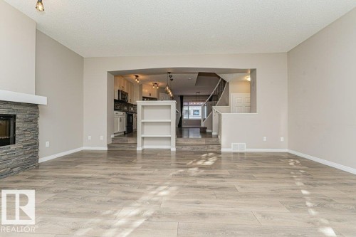 Spacious living area featuring wood-finish flooring, a stacked stone fireplace with a white mantel, and track lighting - 3203 Carpenter Landing Sw, Edmonton, AB 