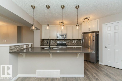 Kitchen featuring white cabinetry, stainless steel appliances, a multi-tone tile backsplash, and a breakfast bar with pendant lighting - 3203 Carpenter Landing Sw, Edmonton, AB 