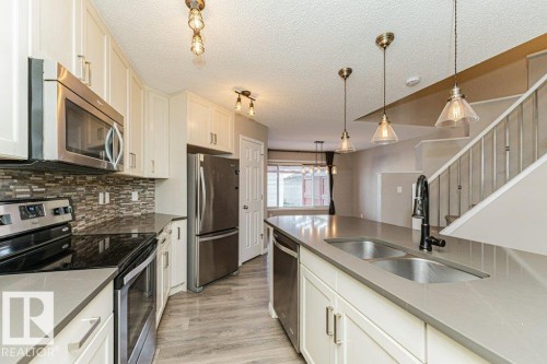 Modern kitchen featuring stainless steel appliances, light-toned cabinetry, light gray countertops, a mosaic tile backsplash, and wood-finish flooring - 3203 Carpenter Landing Sw, Edmonton, AB 