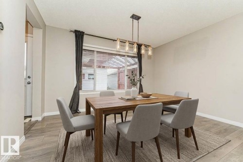 Dining area featuring wood-finish flooring, a window with blinds, and a multi-bulb linear chandelier - 3203 Carpenter Landing Sw, Edmonton, AB 