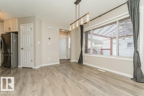 Wood-finish flooring, white trim, recessed lighting, stainless steel refrigerator, and a linear chandelier - 3203 Carpenter Landing Sw, Edmonton, AB 
