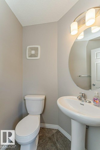 Pedestal sink with chrome fixtures and an oval mirror, complemented by an overhead vanity light fixture - 3203 Carpenter Landing Sw, Edmonton, AB 