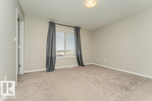 Neutral-toned wall paint, textured ceiling, central window with horizontal blinds, and carpeting - 3203 Carpenter Landing Sw, Edmonton, AB 