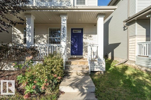Covered front porch with white railing, light-colored siding, and a vibrant blue entry door - 3203 Carpenter Landing Sw, Edmonton, AB 