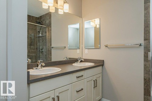 Dual vanity with integrated sinks, a built-in wall mirror, and modern lighting fixture - 3203 Carpenter Landing Sw, Edmonton, AB 