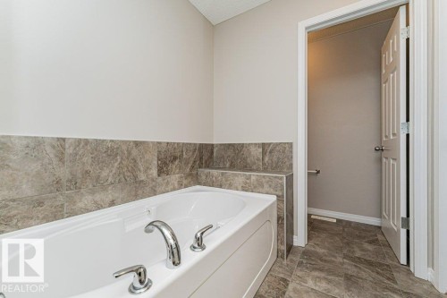 Built-in soaking tub with chrome fixtures, surrounded by large format tile - 3203 Carpenter Landing Sw, Edmonton, AB 