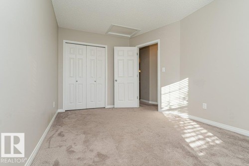 Neutral-toned carpeting and walls, white bi-fold closet doors, white paneled door, and a textured ceiling - 3203 Carpenter Landing Sw, Edmonton, AB 