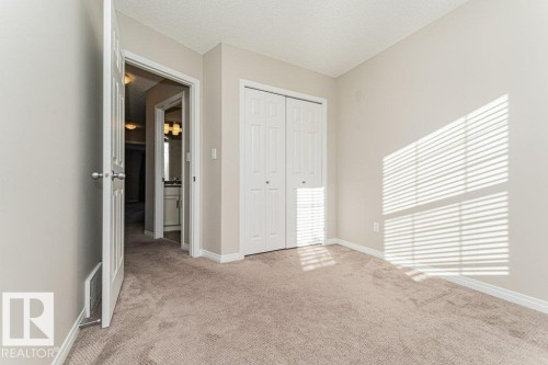 Plush neutral carpeting with white baseboards, a white bi-fold closet, and a white interior door with a brushed nickel knob - 3203 Carpenter Landing Sw, Edmonton, AB 