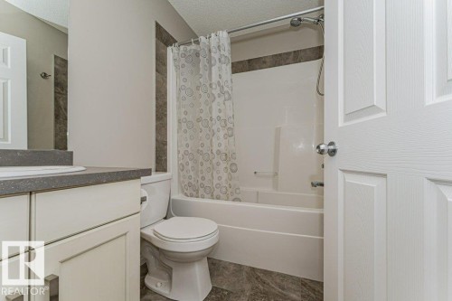 White vanity with brushed nickel hardware, gray countertop with integrated sink, shower-over-tub combination with tiled surround, and dark patterned flooring - 3203 Carpenter Landing Sw, Edmonton, AB 
