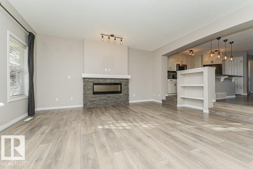 Wood-finish flooring throughout, featuring a stone-clad fireplace with an integrated linear firebox and mantel - 3203 Carpenter Landing Sw, Edmonton, AB 