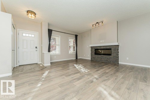 Wood-finish flooring throughout, entry door with window panes, built-in electric fireplace with stone surround, and windows with blinds - 3203 Carpenter Landing Sw, Edmonton, AB 