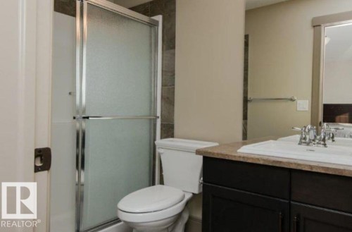 Shower with sliding frosted glass doors, dark wood-finish vanity with countertop, and an integrated sink with a chrome faucet - 7233 Armour Crescent Sw, Edmonton, AB 