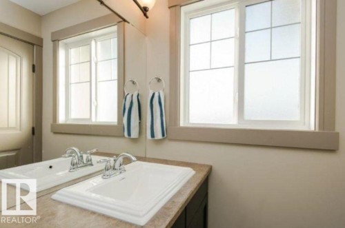 Dual sink vanity with integrated white basins and chrome faucets, complemented by a large wall-mounted mirror - 7233 Armour Crescent Sw, Edmonton, AB 