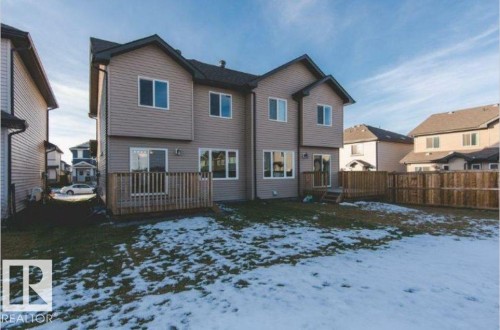 Rear exterior featuring light-toned siding, multiple windows, a wooden deck, and a fenced perimeter - 7233 Armour Crescent Sw, Edmonton, AB 