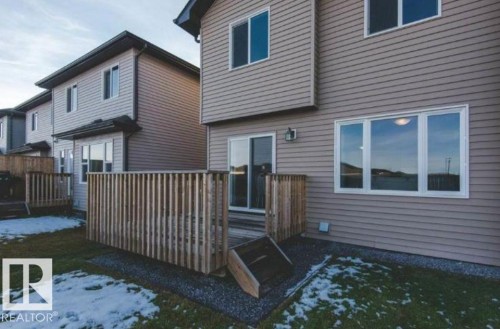 Tan siding exterior with white window frames and a rear deck featuring a wooden privacy screen - 7233 Armour Crescent Sw, Edmonton, AB 