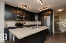 Kitchen featuring dark cabinetry, light-toned countertops, stainless steel appliances, a center island with an integrated sink, and wood-finish flooring - 7233 Armour Crescent Sw, Edmonton, AB 