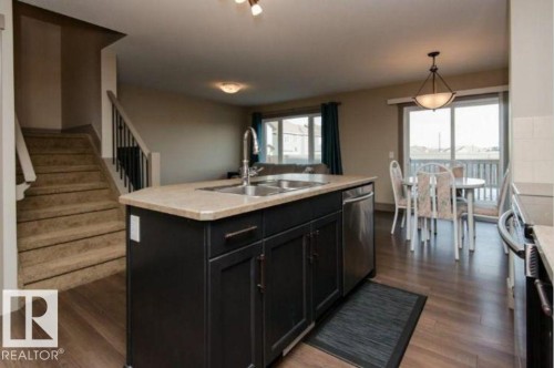 Kitchen island with dark cabinetry, stainless steel dishwasher, and a double-basin sink - 7233 Armour Crescent Sw, Edmonton, AB 
