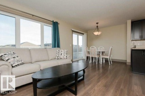 Open-concept living space featuring wood-finish flooring, large windows, a sliding glass door, kitchen cabinetry with a tile backsplash, and a ceiling-mounted light fixture - 7233 Armour Crescent Sw, Edmonton, AB 