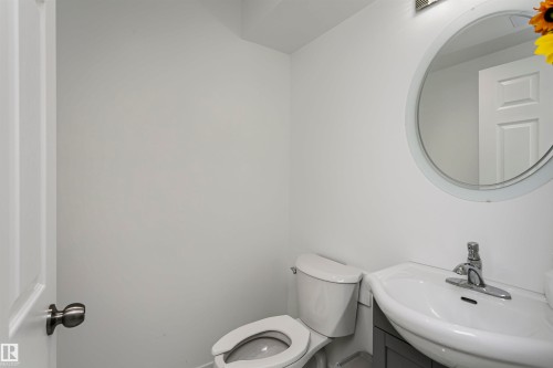 White-painted interior with a round wall mirror, white pedestal sink, and chrome-finish faucet - 7204 92B Avenue Nw, Edmonton, AB 