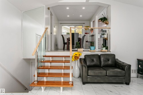 Split-level interior featuring a glass and wood railing staircase, recessed lighting, and a partial wall with wood-finish top - 7204 92B Avenue Nw, Edmonton, AB 