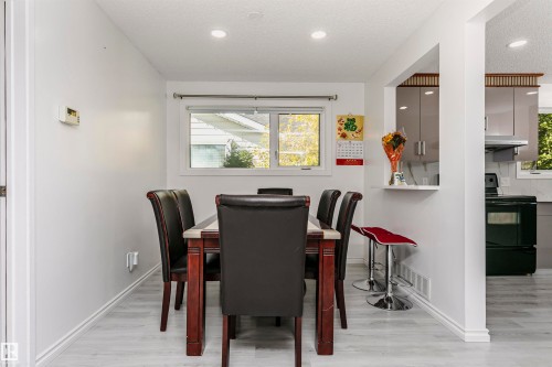 White-painted walls with a window, light wood-finish flooring, and a pass-through opening to the kitchen - 7204 92B Avenue Nw, Edmonton, AB 
