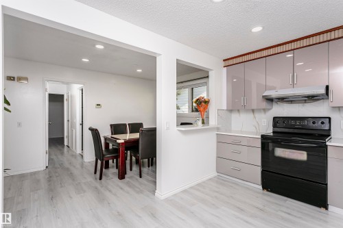Kitchen featuring light-finish cabinetry, a black electric range, a stainless steel range hood, white countertops, and a white backsplash - 7204 92B Avenue Nw, Edmonton, AB 