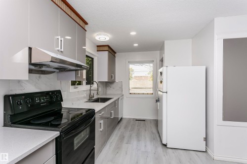 Contemporary kitchen featuring light gray cabinetry, white countertops, a black range, a stainless steel range hood, and light wood-finish flooring - 7204 92B Avenue Nw, Edmonton, AB 