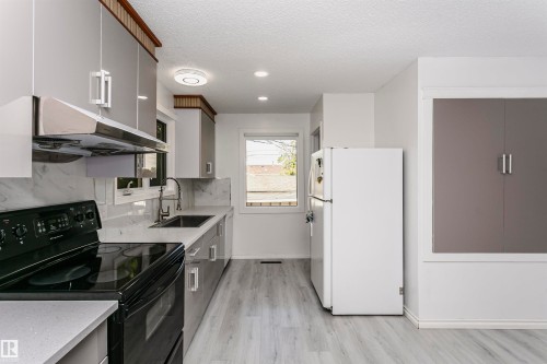 Modern kitchen featuring light wood-finish flooring, white countertops, gray cabinetry, a black electric range, and a stainless steel range hood - 7204 92B Avenue Nw, Edmonton, AB 