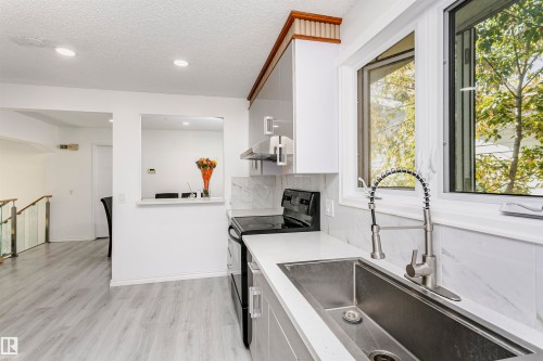 Kitchen featuring light wood-finish flooring, white cabinetry, integrated stainless steel sink, and a multi-pane window - 7204 92B Avenue Nw, Edmonton, AB 