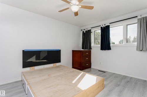 Light wood-finish flooring, ceiling fan with integrated lighting, white walls, and multiple windows - 7204 92B Avenue Nw, Edmonton, AB 