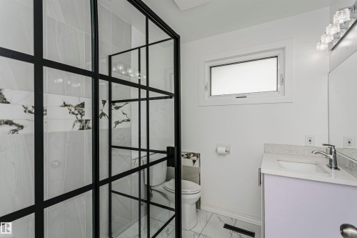 Black-framed glass shower enclosure, white wall tiles with decorative accent, white vanity with integrated sink, chrome faucet, and under-window placement - 7204 92B Avenue Nw, Edmonton, AB 