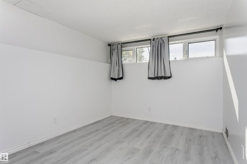 Bright basement room featuring wood-finish flooring, white walls, and dual windows with natural light and privacy curtains - 7204 92B Avenue Nw, Edmonton, AB 