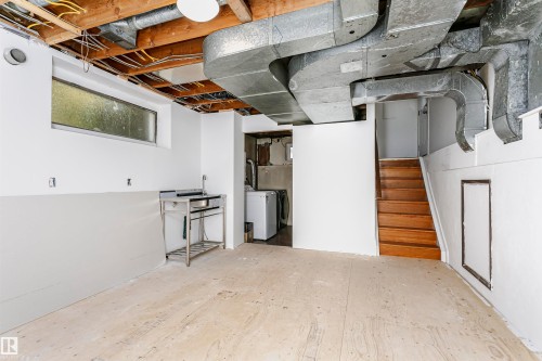 Unfinished basement space featuring exposed wood beams, a horizontal window, and a utility sink - 7204 92B Avenue Nw, Edmonton, AB 