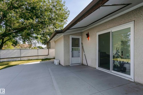 Expansive concrete patio with direct outdoor access, a stucco exterior, and a chain-link fence - 7204 92B Avenue Nw, Edmonton, AB 