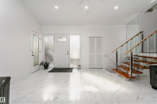 White laminate flooring, modern open-riser staircase with glass railing, recessed lighting, and a paneled front door with frosted sidelights - 7204 92B Avenue Nw, Edmonton, AB 