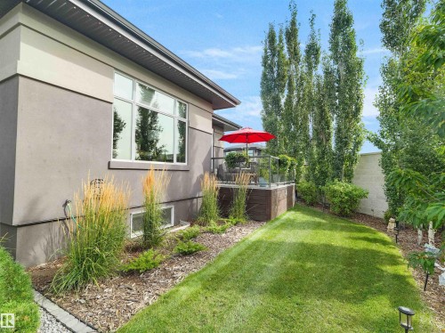 Exterior featuring stucco siding, a raised deck with glass railings, an expansive lawn, and mature trees - 904 Wood Place Nw, Edmonton, AB 