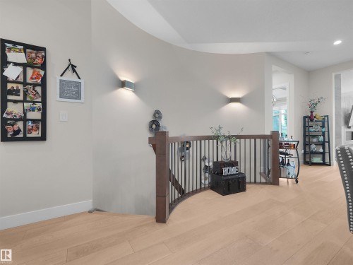 Curved hallway featuring light wood-finish flooring, a dark wood and metal railing, and contemporary wall sconces - 904 Wood Place Nw, Edmonton, AB 
