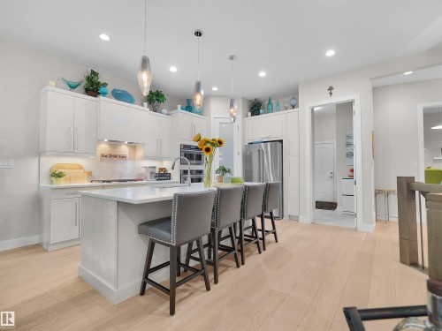 Kitchen featuring light wood-finish flooring, white cabinetry, a large center island with a light-toned countertop, and stainless steel appliances - 904 Wood Place Nw, Edmonton, AB 