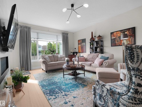 Recessed fireplace with a flat screen mount, light wood-finish flooring, large window with blinds and drapery, and a contemporary ceiling light fixture - 904 Wood Place Nw, Edmonton, AB 