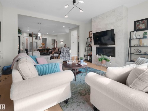 Open-concept living space featuring wood-finish flooring, a contemporary ceiling light fixture, and a fireplace with a stone-tile surround - 904 Wood Place Nw, Edmonton, AB 