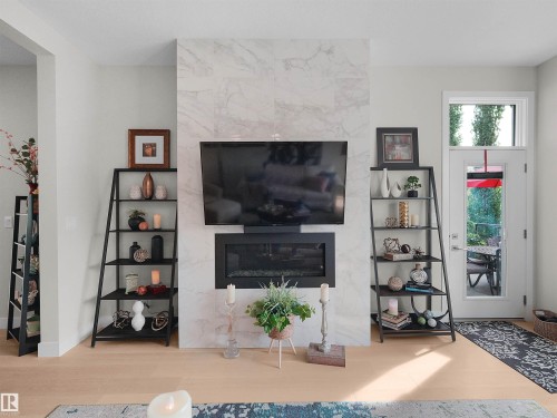 Integrated fireplace with a light-toned surround, wood-finish flooring, and a white door with transom window - 904 Wood Place Nw, Edmonton, AB 