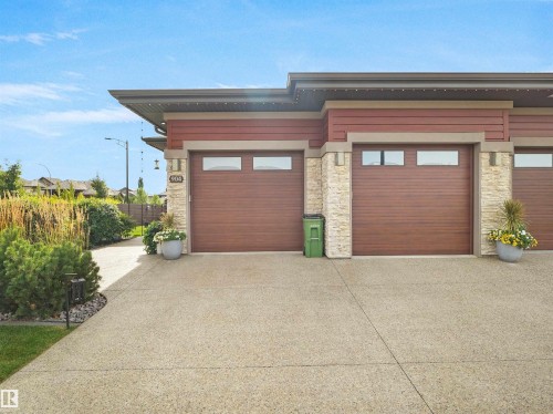 Attached garage with two wood-finish garage doors featuring rectangular windows, stone veneer accents, and a concrete driveway - 904 Wood Place Nw, Edmonton, AB 