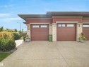 Attached garage with two wood-finish garage doors featuring rectangular windows, stone veneer accents, and a concrete driveway - 904 Wood Place Nw, Edmonton, AB 
