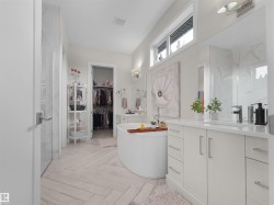 Freestanding soaking tub, dual vanity with undermount sinks, separate glass-enclosed shower, walk-in closet, and light-toned tile flooring in a herringbone pattern - 