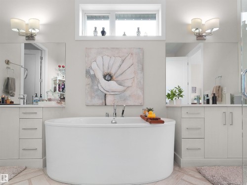 Freestanding oval soaking tub with floor-mounted tub filler, dual vanity sinks with white cabinetry, and a transom window - 904 Wood Place Nw, Edmonton, AB 