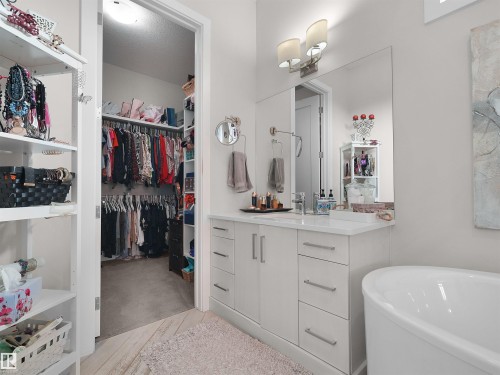Integrated walk-in closet with built-in shelving, spacious vanity with white countertop, chrome fixtures, large wall-mounted mirror, and a freestanding soaking tub - 904 Wood Place Nw, Edmonton, AB 