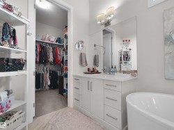 Integrated walk-in closet with built-in shelving, spacious vanity with white countertop, chrome fixtures, large wall-mounted mirror, and a freestanding soaking tub - 