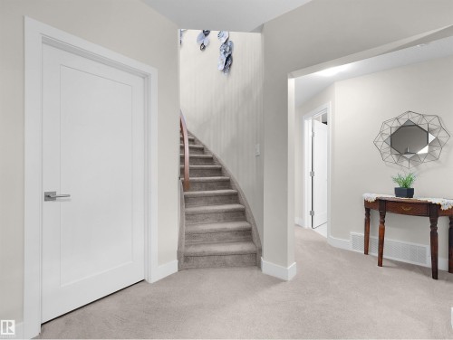 Curved staircase with wood handrail, light-colored carpeting, white interior doors, and arched entryway - 904 Wood Place Nw, Edmonton, AB 