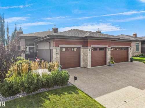 Contemporary exterior with stone accents, wood-finish garage doors, a multi-car driveway, and mature landscaping - 904 Wood Place Nw, Edmonton, AB 